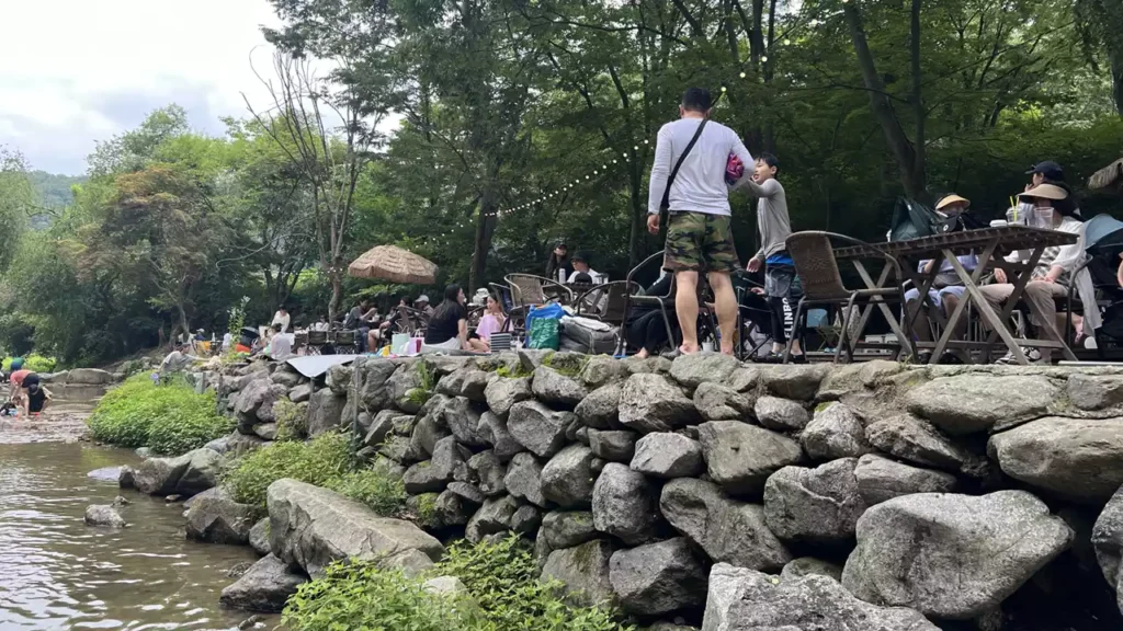 남한산성-개울가-테이블-자리-피크닉-가족-물놀이 계곡 옆 테이블에서 쉬는 사람들과 개울에서 노는 가족들